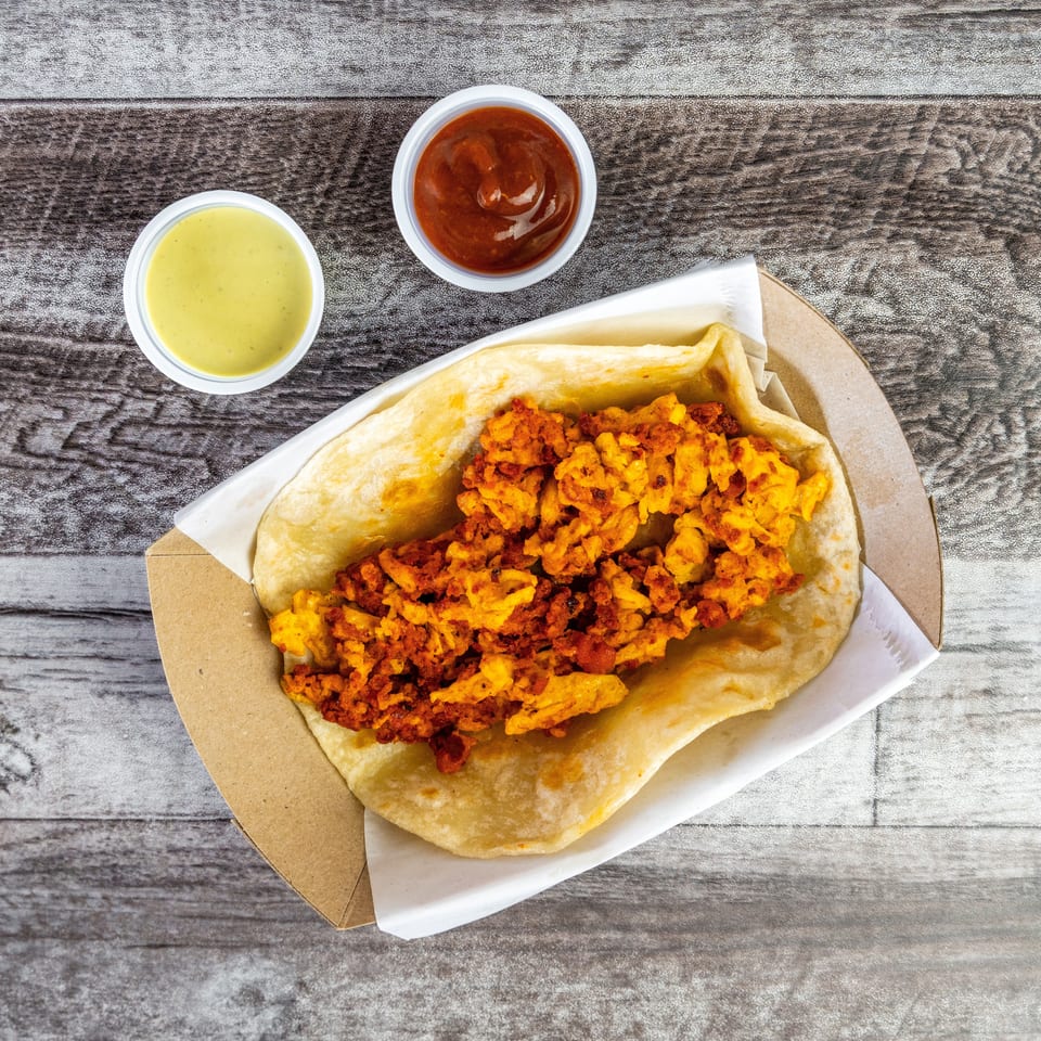 Open flatbread filled with crispy golden fried pieces, served in a paper tray with green and red dipping sauces.