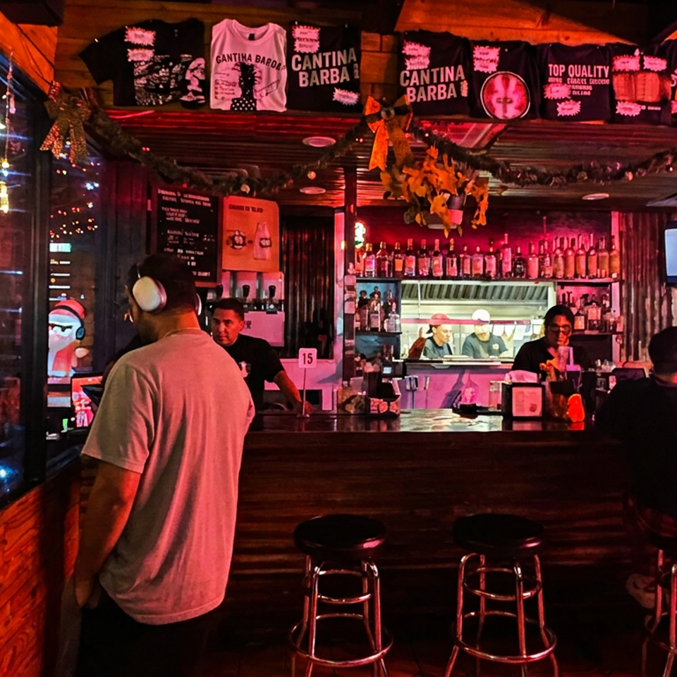 Festively decorated Cantina Barba bar with patrons, liquor shelves, counter seating, and branded merchandise under red lighting.