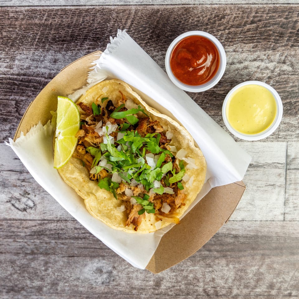 Two tacos topped with shredded meat, onions, and cilantro, served with lime and red and yellow sauces.