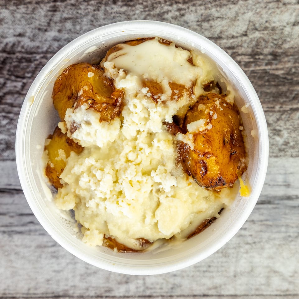 Close-up of roasted potatoes topped with creamy mashed potatoes and melted cheese in a clear bowl.