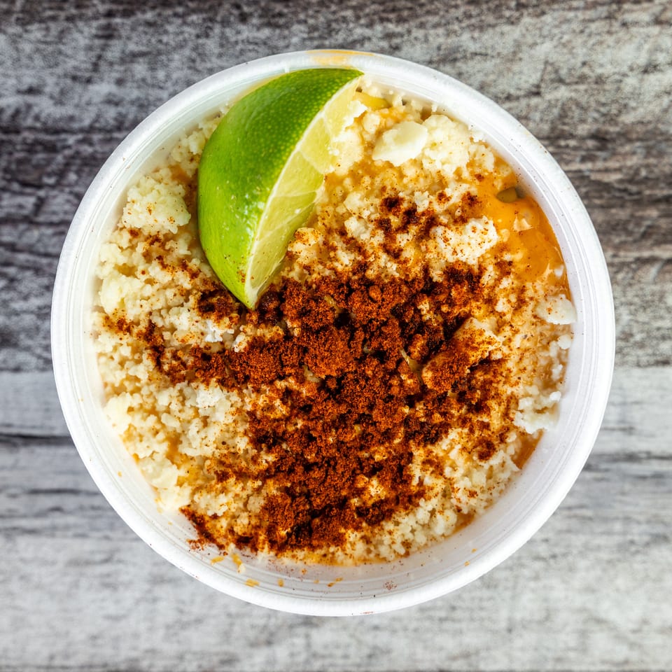 Overhead view of a creamy, spice-topped dish in a takeout container, garnished with a lime wedge.