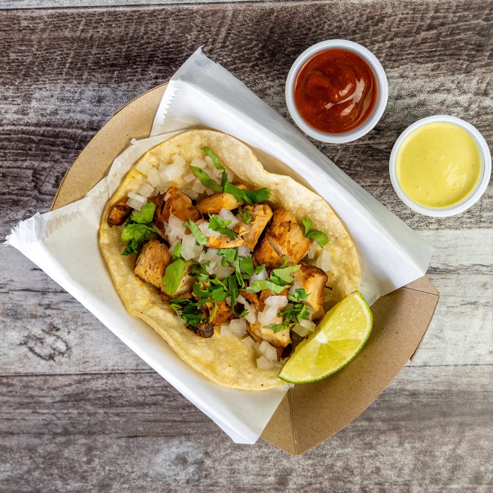 Grilled chicken tacos topped with chopped onions and cilantro, served with lime wedges and red and yellow sauces.