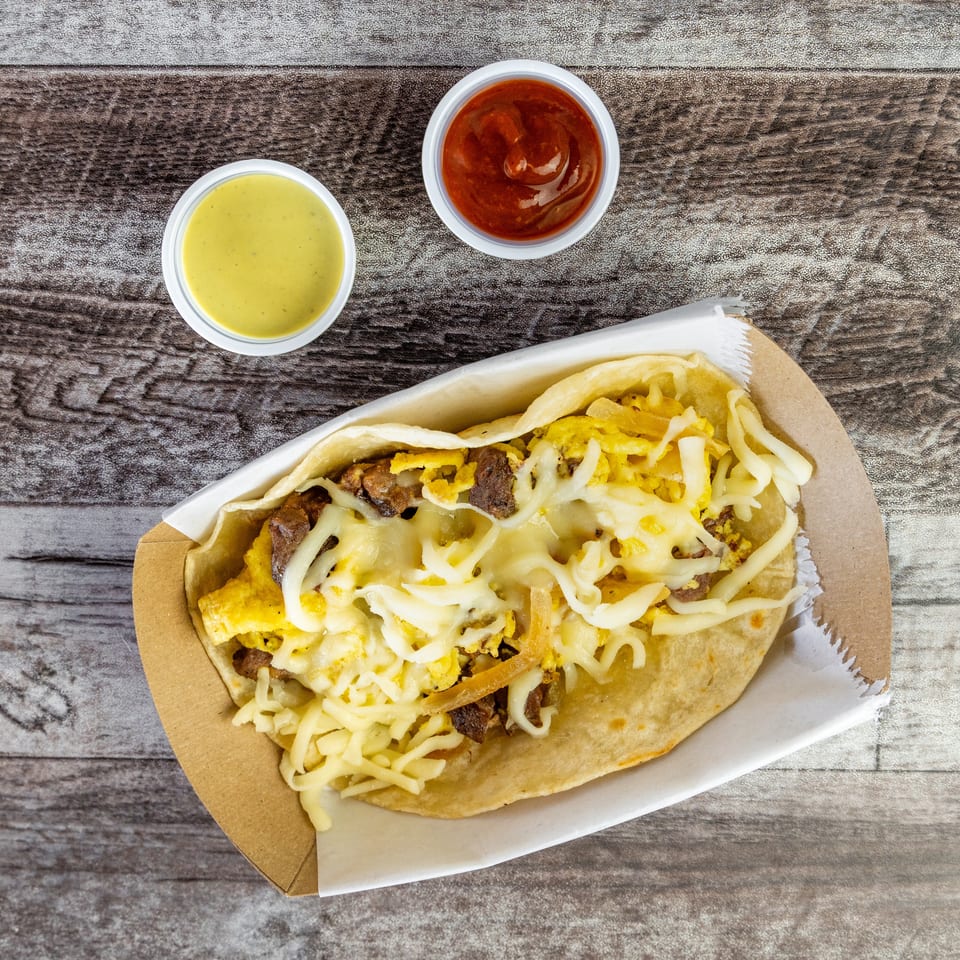 Loaded flatbread wrap with scrambled eggs, grilled meat, onions, and melted cheese, served with yellow and red dipping sauces.