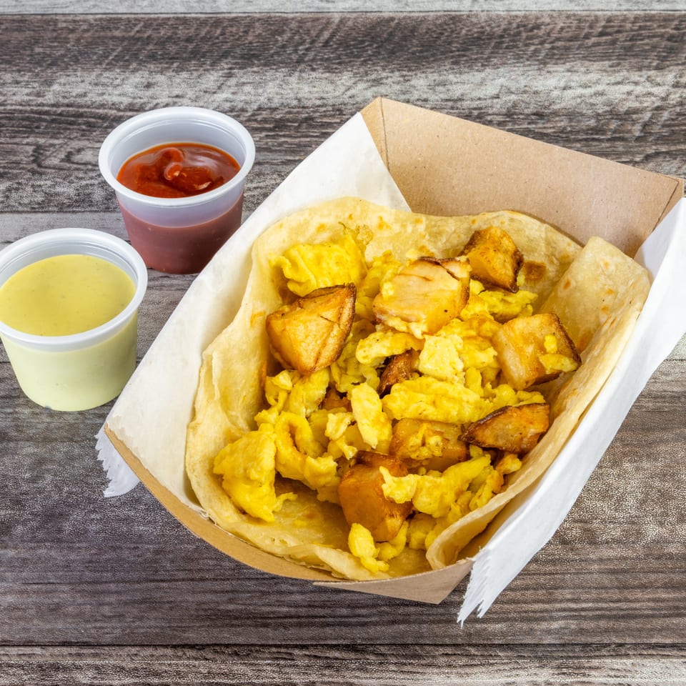 Basket of scrambled eggs, roasted potatoes, and flatbread served with red and creamy green sauces on a wooden table.