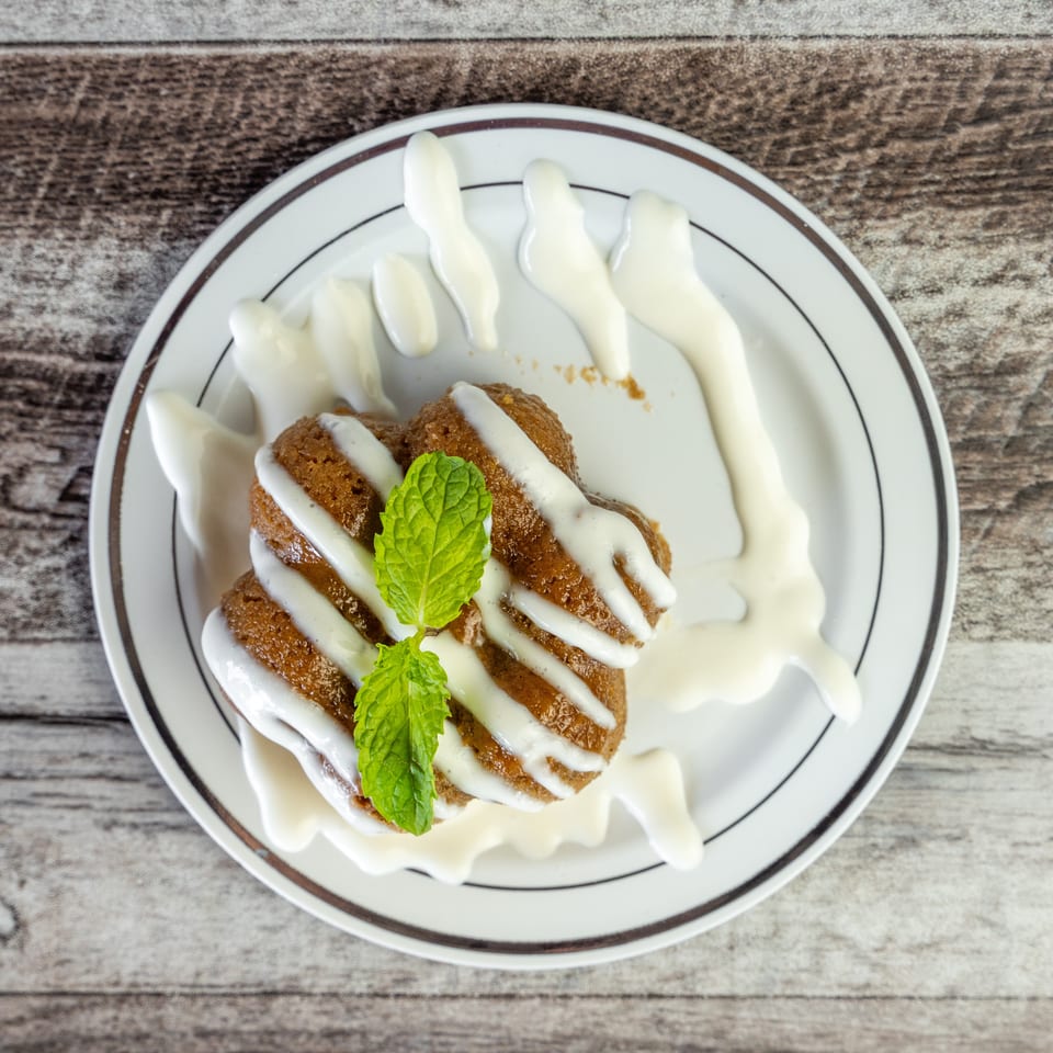 Sliced golden-brown dessert drizzled with white sauce and garnished with fresh mint on a decorative plate.