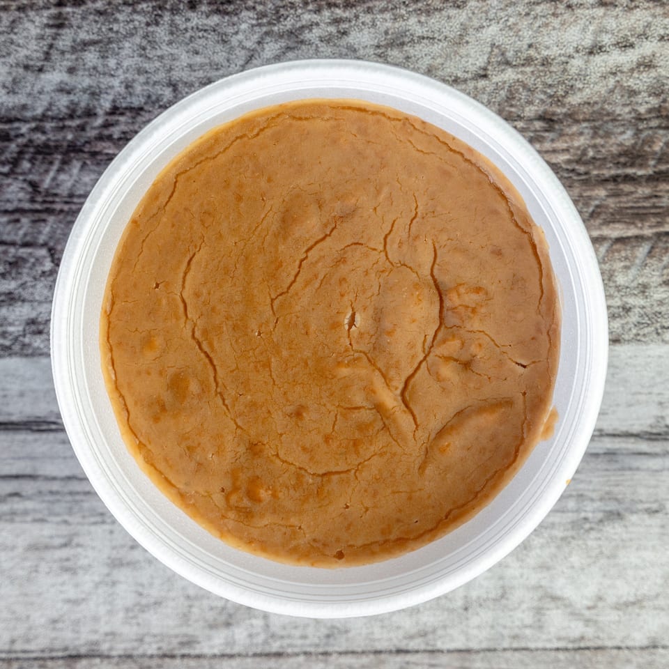 Top-down view of a round golden-brown dessert with a cracked surface in a clear plastic container on a wooden table.
