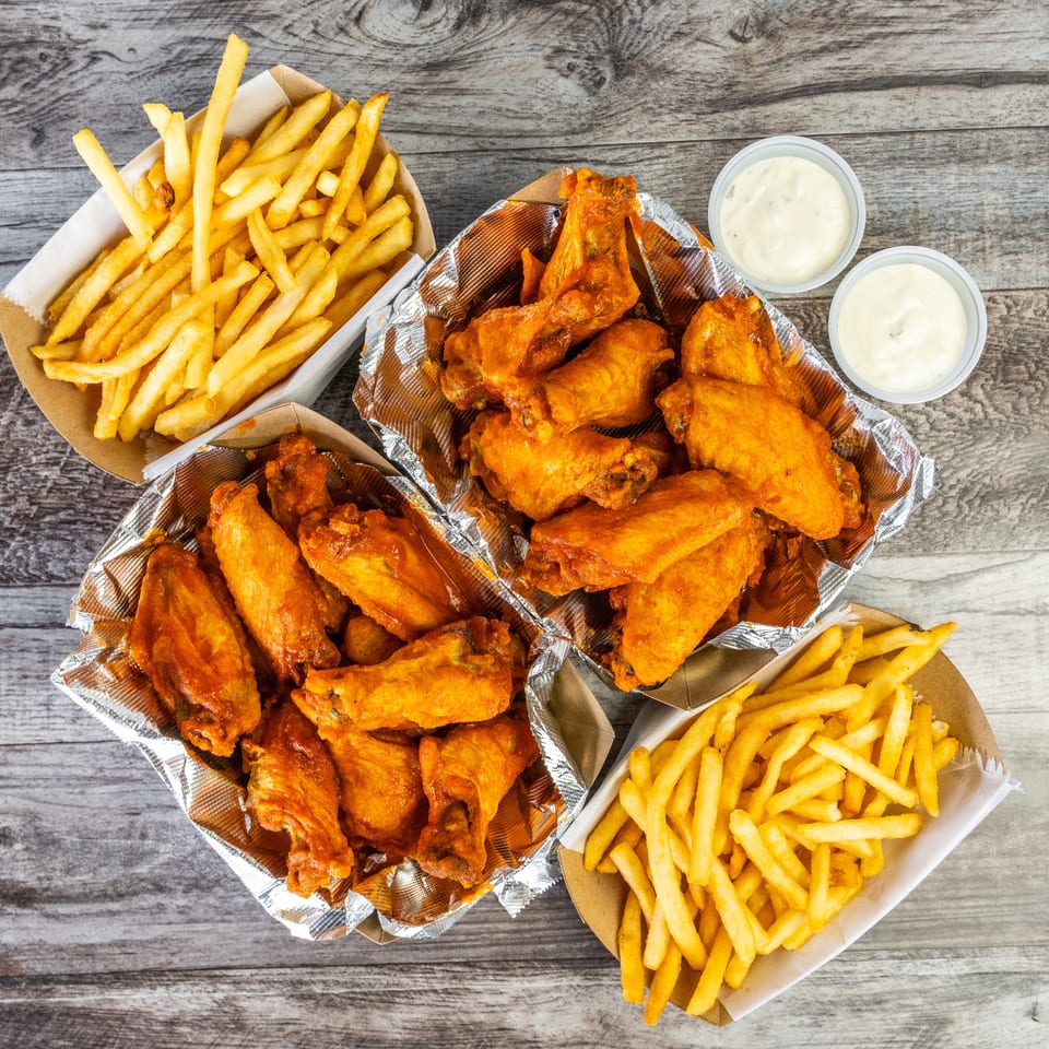 Overhead view of crispy chicken wings, French fries, and two cups of creamy dipping sauce on a wooden table.