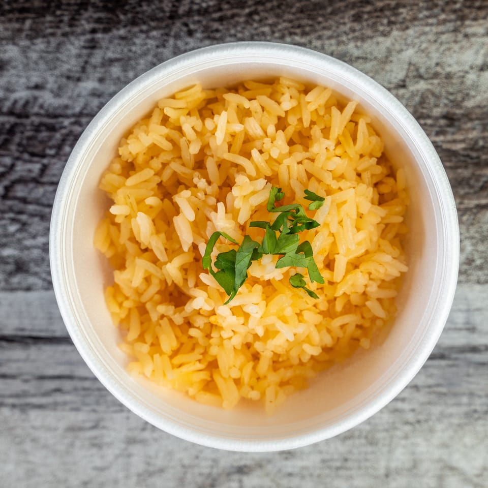 Close-up of yellow seasoned rice garnished with fresh cilantro in a round takeaway container on a gray wood surface.