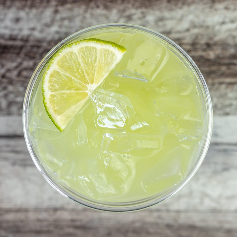 Top-down view of a pale green iced lime drink garnished with a lime wedge on a rustic wooden table.